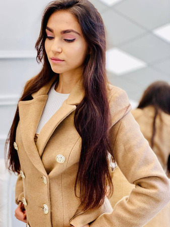 Krótki, elegancki beżowy dwurzędowy płaszcz PRESTIGE la Femme, zapinany na złote guziki.