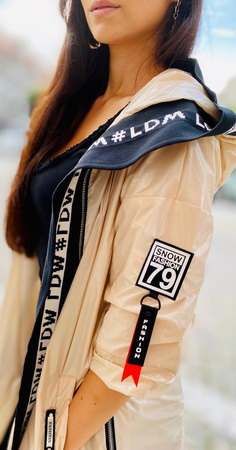 Długa, beżowa kurtka parka BEIGE NORBI, zdobiona czarnym wykończeniem, zapinana na zamek z kapturem.